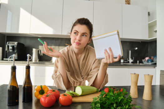 Woman thoughtfully planning meals with fresh fruits, vegetables, and a notebook for cycle syncing diet