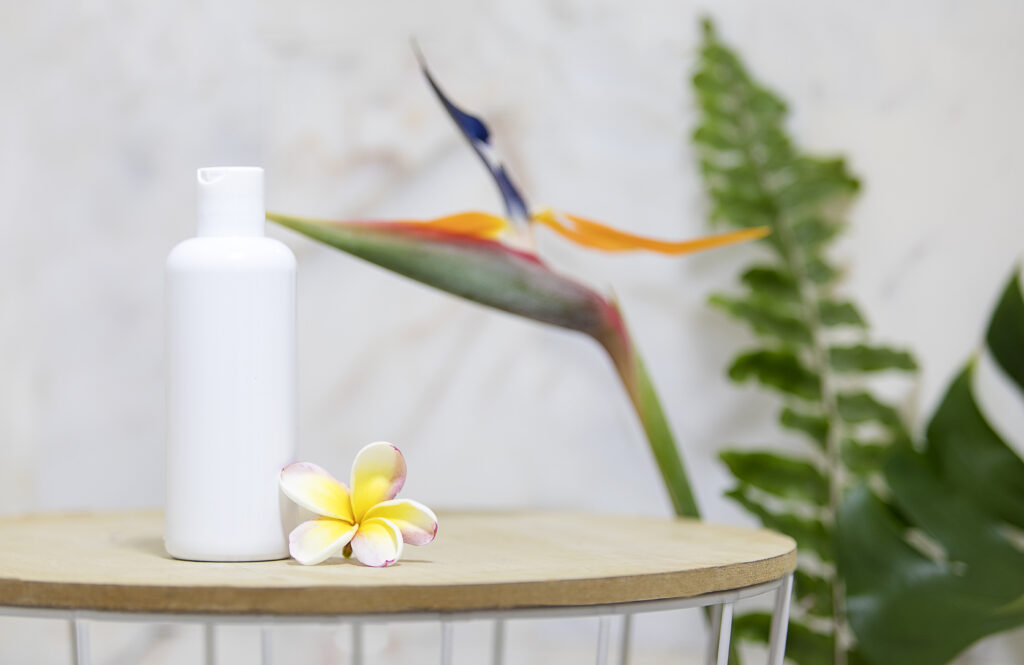 Table with a clear white bottle and green palm leaves over a marble wall.