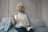 A woman in her 50s sitting on a sofa with a cup of tea, looking thoughtful and calm about perimenopause and menopause
