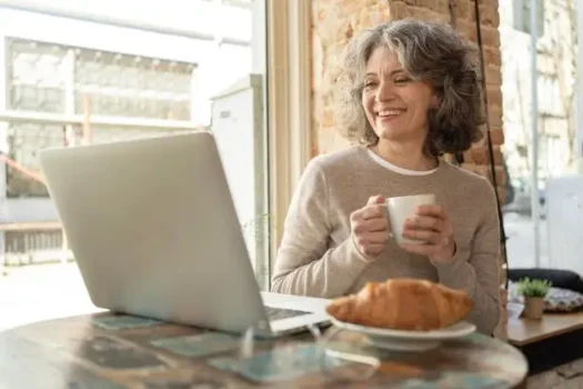 A smiling woman in her late 40s looks at a tablet, representing accessible telehealth for menopause relief
