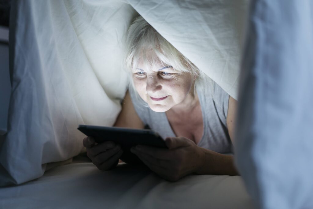 A senior woman fighting with menopause and insomnia, scrolling on her tablet during the night